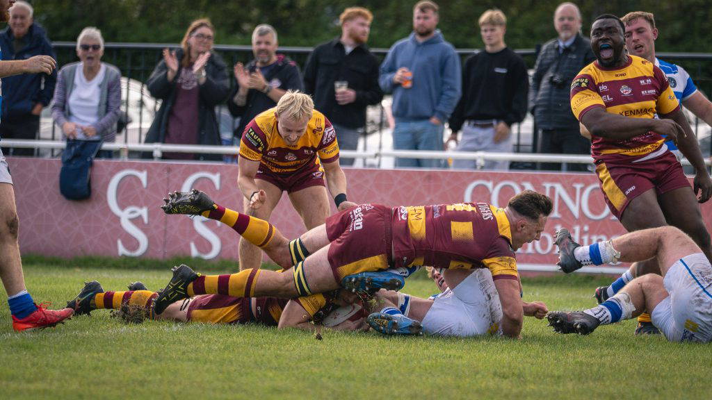 A Sedgley Park Tigers player grounds the ball for a try as teammates and the Park Lane crowd celebrate