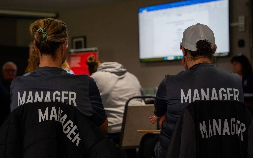 Two Sedgley Park team managers in club gilets watching the presentation at the managers training evening