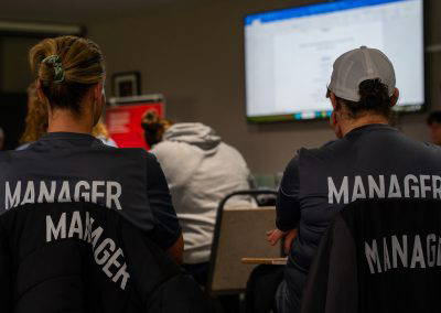 Two Sedgley Park team managers in club gilets watching the presentation at the managers training evening
